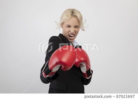 Angry young businesswoman in boxing gloves ready for fight over light grey background, preparing for combat 87021697