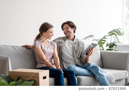 Glad happy young caucasian husband in glasses and wife in casual relaxing on sofa with tablet, planning new interior Glad happy young caucasian husband in glasses and wife in casual relaxing on sofa with tablet, planning new interior 87021998