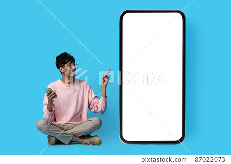 Happy indian guy pointing at huge smartphone with blank screen 87022073