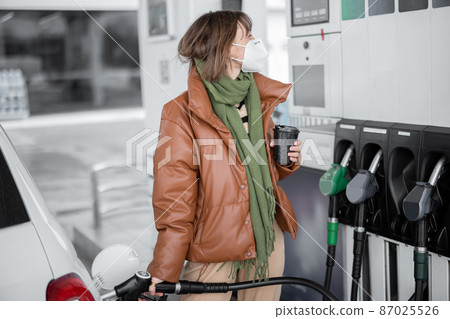 Woman in mask refueling car with gasoline at gas station 87025526