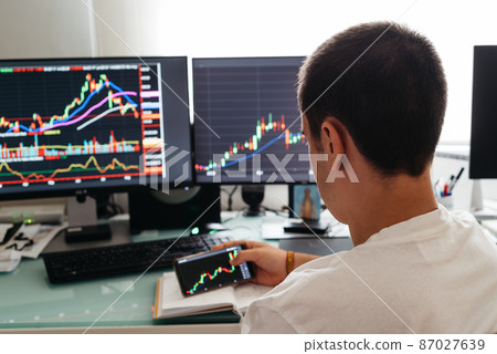Successful young trader in casual wear working with charts and market reports at home 87027639