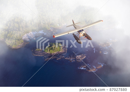 Seaplane Flying over the West Coast Pacific Ocean at sunset. 87027880
