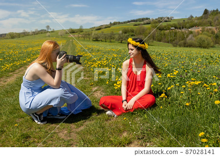 Young girl is posing photographing friend on dandelion meadow 87028141