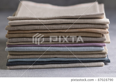 A pile of four folded dull-colored natural linen fabric, close up 87028790