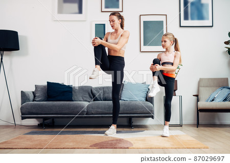 Mother and daughter working out at home, doing stretching exercises Mother and daughter working out at home, doing stretching exercises 87029697
