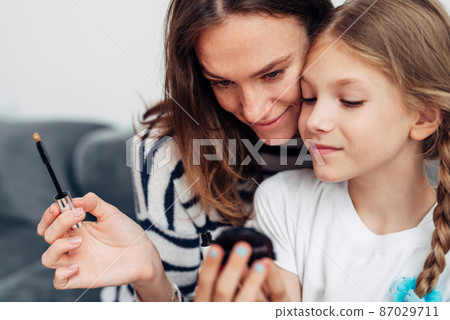 Mother and daughter doing makeup and admiring in a small mirror Mother and daughter doing makeup and admiring in a small mirror 87029711