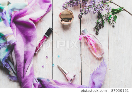 Flat lay, top view spring table desk frame. Feminine desk workspace with cosmetics, lipstick and lilac flowers on wooden background. 87030161