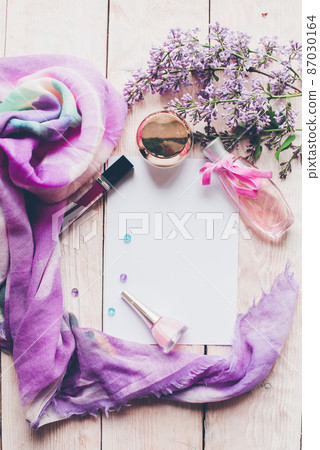 Flat lay, top view spring table desk frame. Feminine desk workspace with cosmetics, lipstick and lilac flowers on wooden background. Flat lay, top view spring table desk frame. Feminine desk workspace with cosmetics, lipstick and lilac flowers on wooden background. 87030164