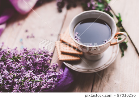 Morning cup of tee, cookies, and lilac flower on wooden table from above. Beautiful breakfast. Flat lay style with copy space 87030250