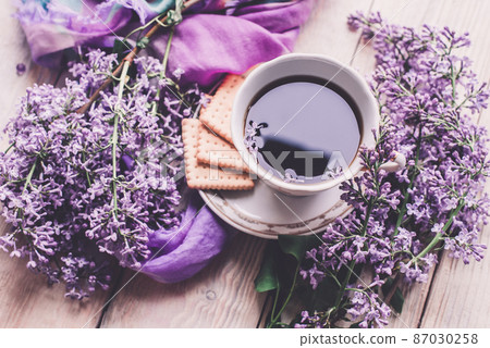 Morning cup of tee, cookies, and lilac flower on wooden table from above. Beautiful breakfast. Flat lay style with copy space Morning cup of tee, cookies, and lilac flower on wooden table from above. Beautiful breakfast. Flat lay style with copy space 87030258