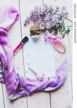 Flat lay, top view spring table desk frame. Feminine desk workspace with cosmetics, lipstick and lilac flowers on wooden background. Flat lay, top view spring table desk frame. Feminine desk workspace with cosmetics, lipstick and lilac flowers on wooden background. 87030300