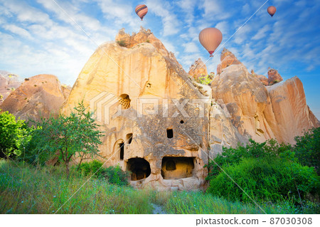 Rock monastery in the Zelve valley under blue sky with hot air balloons 87030308