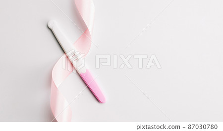 Pregnancy test kit. Positive woman pregnant test with pink silk ribbon on white background. New life and new family. Motherhood, pregnancy, birth control concept. 87030780