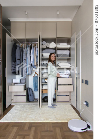 Joyful female putting box on shelf in cupboard enjoying housework at wardrobe organizing storage Joyful female putting box on shelf in cupboard enjoying housework at wardrobe organizing storage 87031885