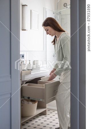 Housewife hands putting rolled up towel into drawer under sink. Organizing storage space in bathroom 87031890