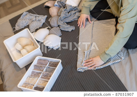 Young woman organizing underwear storage at bedroom. Contemporary folded container cases clothing Young woman organizing underwear storage at bedroom. Contemporary folded container cases clothing 87031907