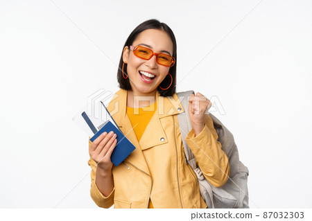 Happy asian girl going on vacation, holding passport and flight tickets, backpack on shoulder. Young woman tourist travelling abroad, standing over white background 87032303
