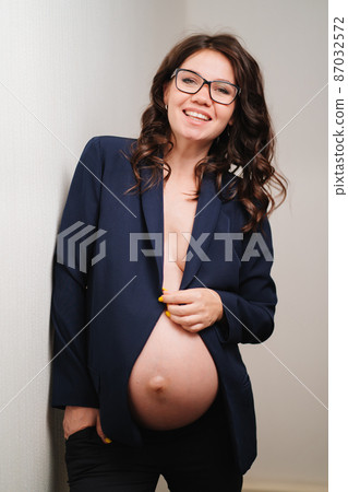 happy pregnant woman in glasses and black jacket with bare breasts and belly happy pregnant woman in glasses and black jacket with bare breasts and belly 87032572