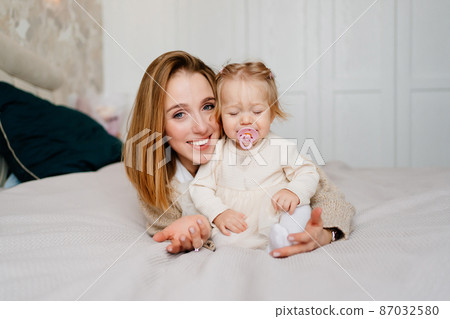 mom and baby daughter with baby nipple play and hug in bed. games with children. 87032580