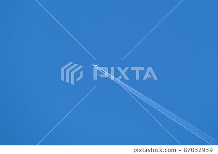 Distant passenger jet plane flying on high altitude on clear blue sky leaving white smoke trace of contrail behind. Air transportation concept Distant passenger jet plane flying on high altitude on clear blue sky leaving white smoke trace of contrail behind. Air transportation concept 87032939