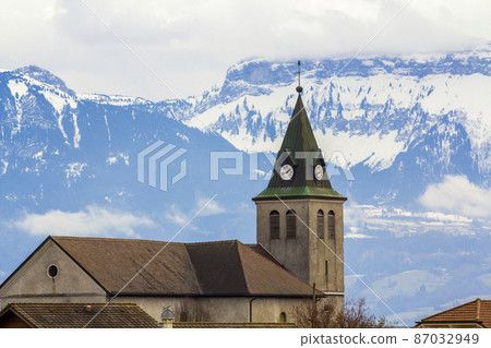 Dark contrast silhouette of church roof with tower against magnificent Alps mountains, Germany. Quiet life on fantastic peaks with shiny snow under bright blue sky with puffy white clouds background. Dark contrast silhouette of church roof with tower against magnificent Alps mountains, Germany. Quiet life on fantastic peaks with shiny snow under bright blue sky with puffy white clouds background. 87032949