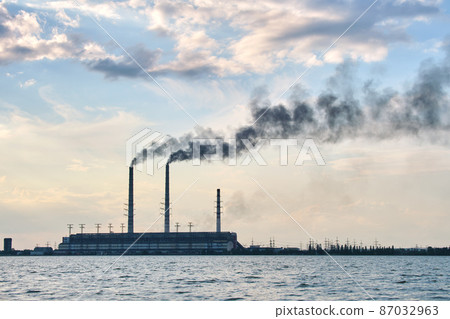 Coal power plant high pipes with black smoke moving upwards polluting atmosphere over lake water Coal power plant high pipes with black smoke moving upwards polluting atmosphere over lake water 87032963