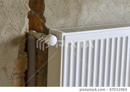 Close-up side view of isolated installed heating radiator on brick rough plastered wall in an empty room of a newly built apartment or house. Construction, maintenance, plumbing and repairing concept. Close-up side view of isolated installed heating radiator on brick rough plastered wall in an empty room of a newly built apartment or house. Construction, maintenance, plumbing and repairing concept. 87032969