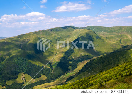 Bright landscape with grassy green meadow and distant mountain hills in summer 87033364