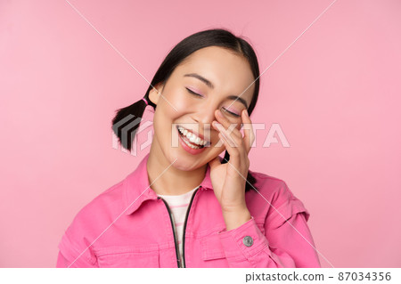 Close up portrait of beautiful asian girl looking enthusiastic and smiling, laughing and smiling, standing happy against pink background Close up portrait of beautiful asian girl looking enthusiastic and smiling, laughing and smiling, standing happy against pink background 87034356