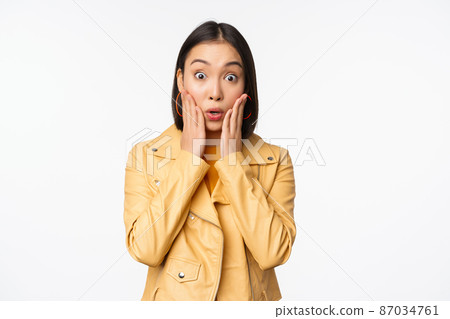 Image of asian woman looking surprised, amazed reaction, shocked face, standing over white background 87034761