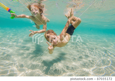Cute boys swimming underwater in shallow turquoise water at tropical beach Cute boys swimming underwater in shallow turquoise water at tropical beach 87035172