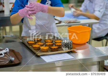 Woman holding piping bag and making cakes with fruit jams 87036409