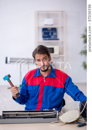 Young male repairman repairing air-conditioner Young male repairman repairing air-conditioner 87036596