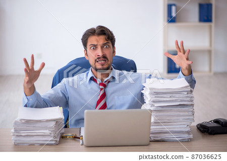 Young male employee and too much work in the office Young male employee and too much work in the office 87036625