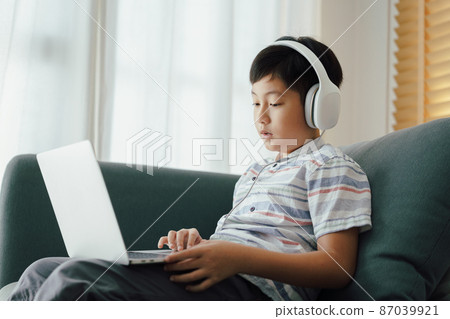 Asian little boy video call online via the internet tutor on a computer laptop with headphone. Asian little boy video call online via the internet tutor on a computer laptop with headphone. 87039921