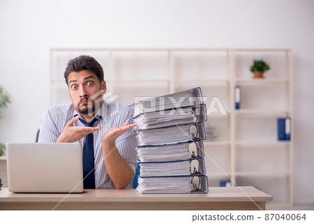 Young male employee and too much work in the office Young male employee and too much work in the office 87040064