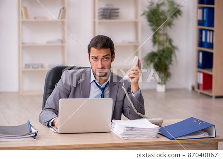 Young male employee unhappy with excessive work in the office Young male employee unhappy with excessive work in the office 87040067