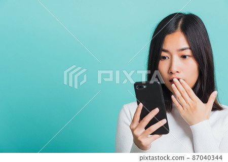 woman surprised shocked with mobile phone close mouth with palm woman surprised shocked with mobile phone close mouth with palm 87040344