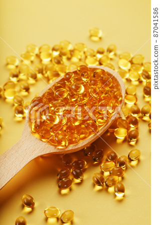 Vitamin D3 Capsules in a spoon with other vitamin D3 capsules around them on a yellow background 87041586