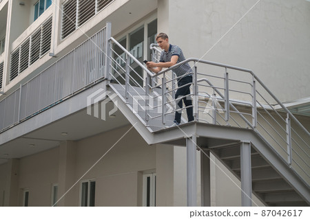 Young caucasian man in casual clothes standing outdoors on the stairs and looking at his phone. Using smartphone. High quality photo 87042617