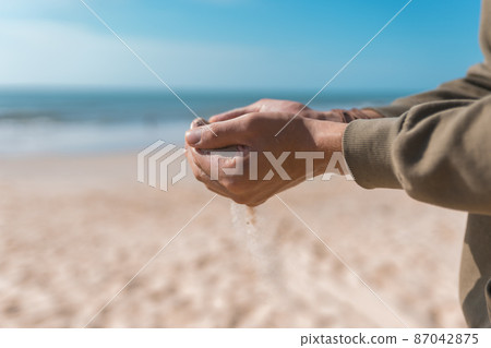 Man holding white sand in his hands. Male palms with the sand on the beach. Sand pouring. Casual hoodie. High quality photo Man holding white sand in his hands. Male palms with the sand on the beach. Sand pouring. Casual hoodie. High quality photo 87042875