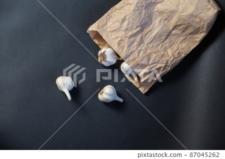 Brown paper bag with garlic against a black background. Heads of ripe garlic in the peel. Close-up. Selective focus Brown paper bag with garlic against a black background. Heads of ripe garlic in the peel. Close-up. Selective focus 87045262