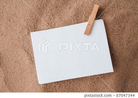 Sheet of white paper with copy space clothespin on sand. Summer vacation holiday concept. Planning trip. Sea time Advertising promotion mock up 87047344