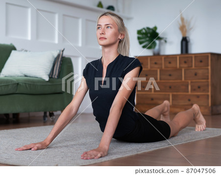 Young woman working out at home, lying on the floor and arching her back. 87047506