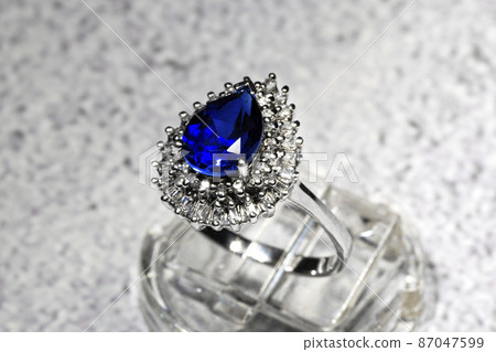 close-up white gold jewelry ring with a large blue pear-cut sapphire and diamonds on a gray background 87047599