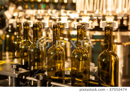Unlabeled glass bottles in bottling machine at modern winery 87050474