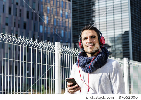 Young man listening music by headphones while holding a mobile phone outdoor Young man listening music by headphones while holding a mobile phone outdoor 87052000