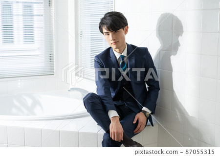 Portrait of a young man in a suit sitting on the edge of a bathtub Portrait of a young man in a suit sitting on the edge of a bathtub 87055315