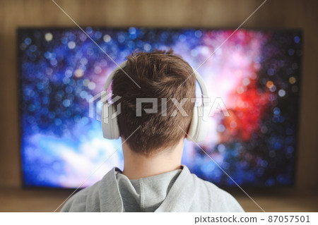 Boy in headphones watching television, teenager boy playing video game in front of screen at home Boy in headphones watching television, teenager boy playing video game in front of screen at home 87057501