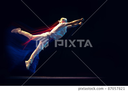 Portrait of man in sports white suit, hip-hop dancer flying isolated on dark background in mixed neon light. Youth culture, hip-hop, movement, style and fashion, action. 87057821